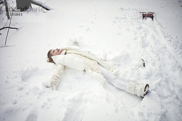 Kaukasisches Mädchen macht Schneeengel auf einem Feld