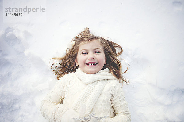 Lächelndes kaukasisches Mädchen liegt im Schnee