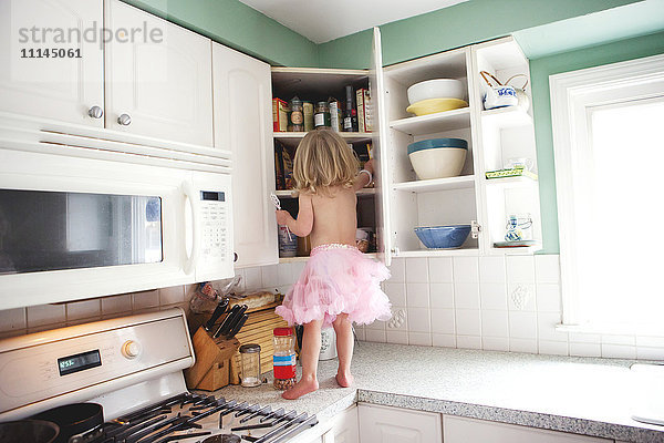 Halbnacktes Mädchen schaut in den Schrank auf der Küchentheke