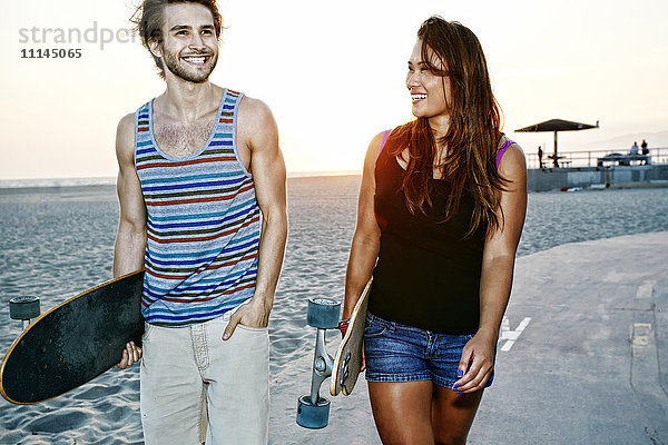 Pärchen mit Skateboards am Strand