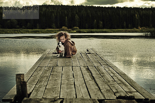 Kaukasisches Mädchen mit Hund auf Holzdeck in ruhigem See