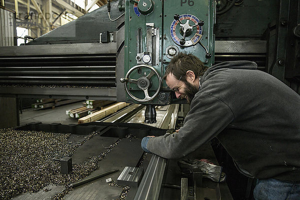 Weißer Mann arbeitet an Maschinen in einer Metallwerkstatt
