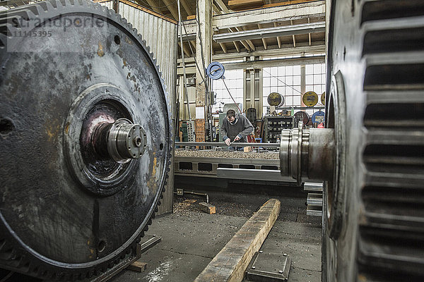 Kaukasischer Mann arbeitet hinter Metallzahnrädern in einer Metallwerkstatt