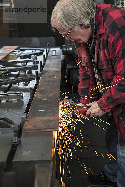 Kaukasischer Mann schleift Metall in einer Metallwerkstatt