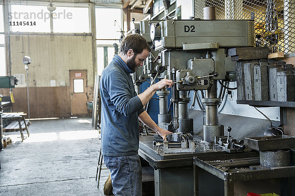 Kaukasischer Mann mit Bohrmaschine in Metallwerkstatt