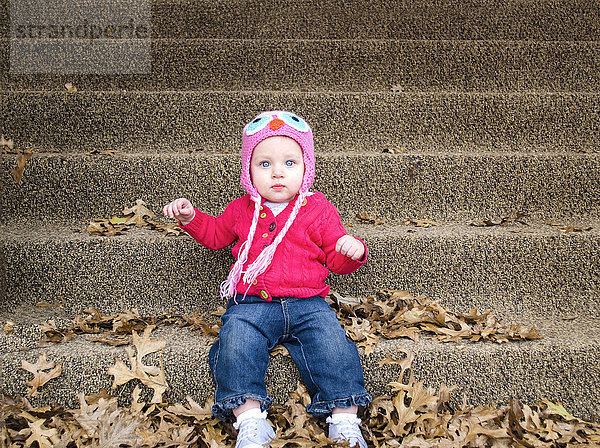 Baby-Mädchen sitzt im Herbst Blätter auf vorderen Stufen