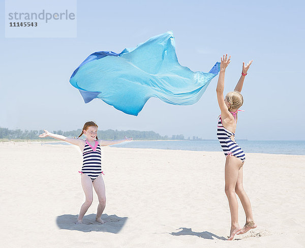 Kaukasische Mädchen spielen mit Stoff am Strand