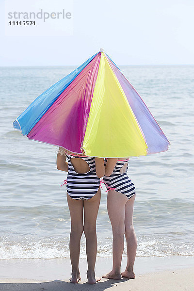 Kaukasische Mädchen unter Regenschirm am Strand