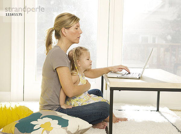 Mutter und Tochter benutzen einen Laptop im Wohnzimmer