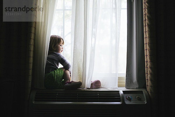Gemischtrassiges Mädchen sitzt im Fenster