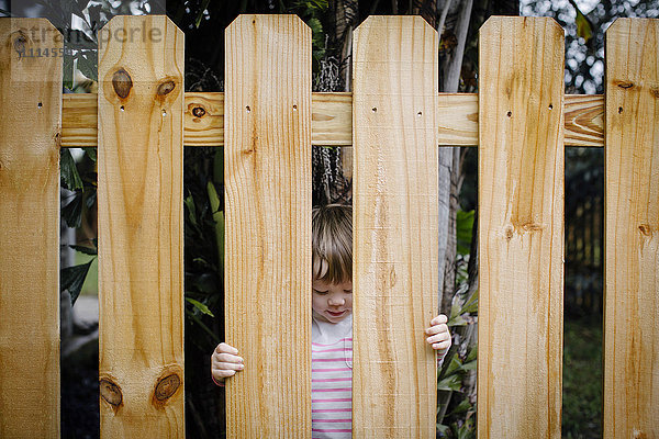 Gemischtrassiges Mädchen schaut durch den Holzzaun im Hinterhof
