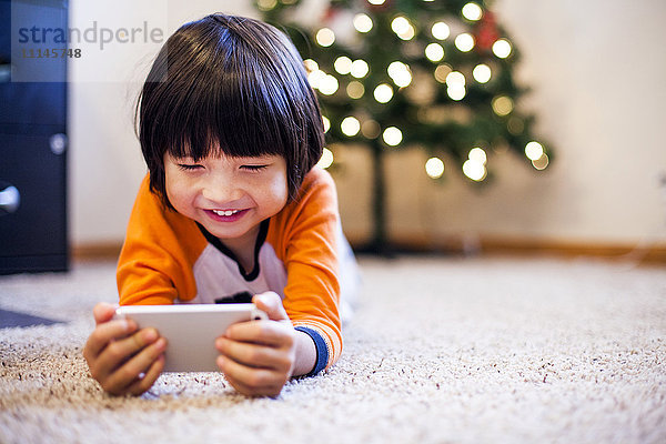 Gemischtrassiger Junge spielt mit Smartphone im Wohnzimmer