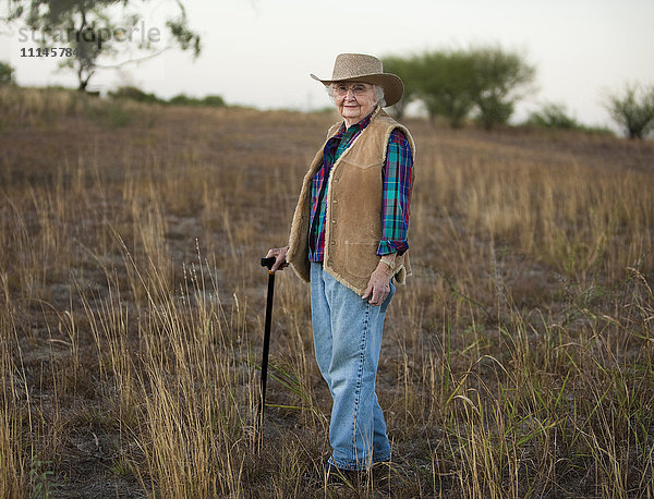 Ältere kaukasische Frau geht mit Stock in einem Feld
