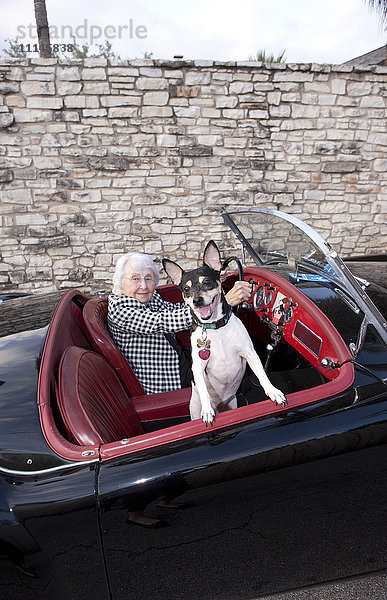 Ältere Frau fährt Cabrio mit Hund