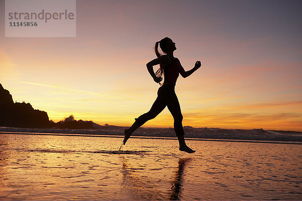 Silhouette einer Frau  die bei Sonnenuntergang am Strand läuft