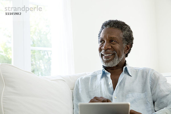 Älterer Mann mit digitalem Tablet auf dem Sofa