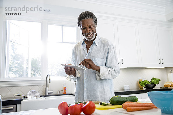 Älterer Mann benutzt digitales Tablet in der Küche