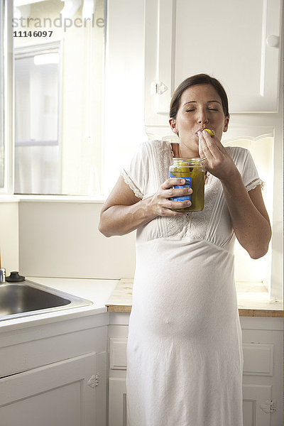 Schwangere Frau isst Essiggurken in der Küche