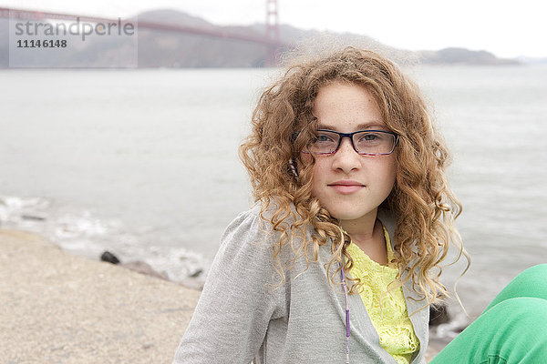 Kaukasisches Mädchen sitzt am Strand in der Nähe der Golden Gate Bridge  San Francisco  Kalifornien  Vereinigte Staaten