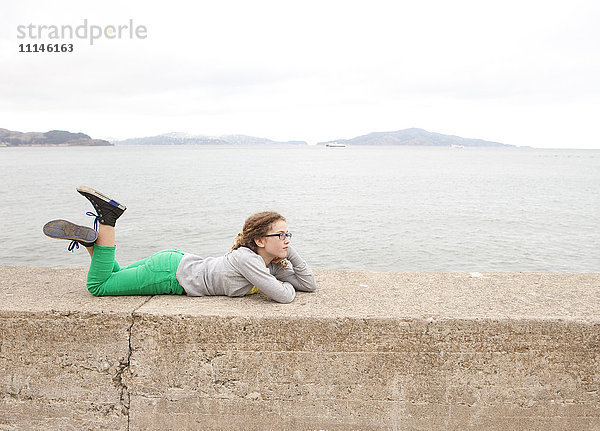 Kaukasisches Mädchen liegt auf einer Betonmauer über dem Meer