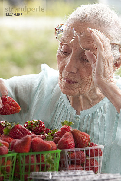 Ältere kaukasische Frau begutachtet Erdbeeren auf dem Bauernmarkt