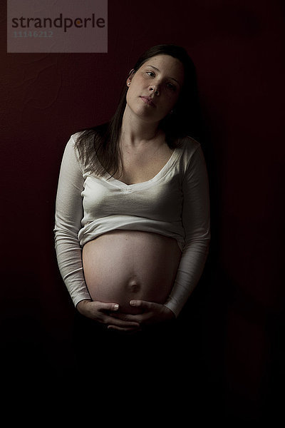 Ernste schwangere Frau  die ihren Bauch hält