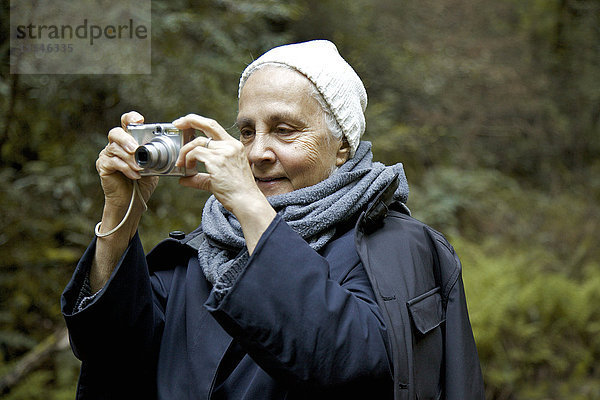 Nahaufnahme einer älteren Frau beim Fotografieren im Wald