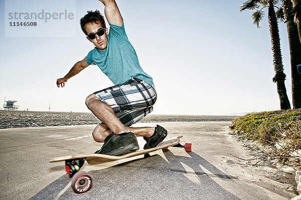 Kaukasischer Mann fährt Longboard am Strand