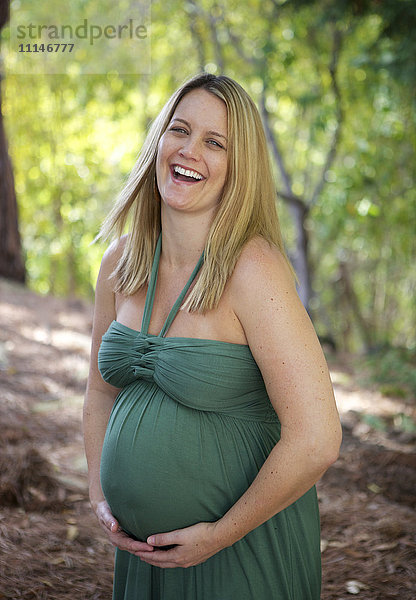 Lachende schwangere Frau  die ihren Bauch hält