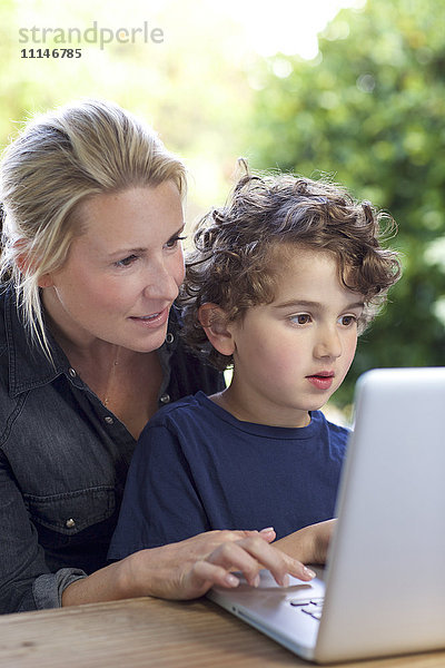 Mutter und Sohn benutzen Laptop am Tisch