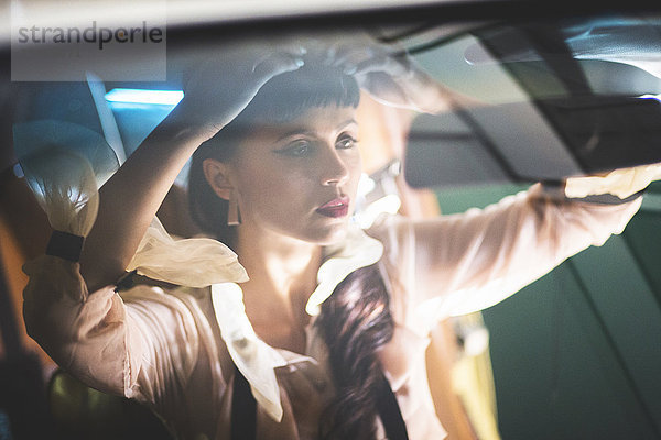 Glamouröse gemischtrassige Frau  die ihr Haar im Autospiegel überprüft