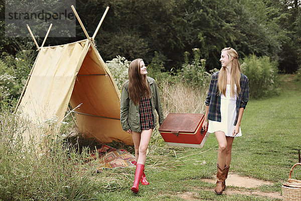 Frauen tragen Vintage-Kühlbox in der Nähe von Camping-Zelt im Wald