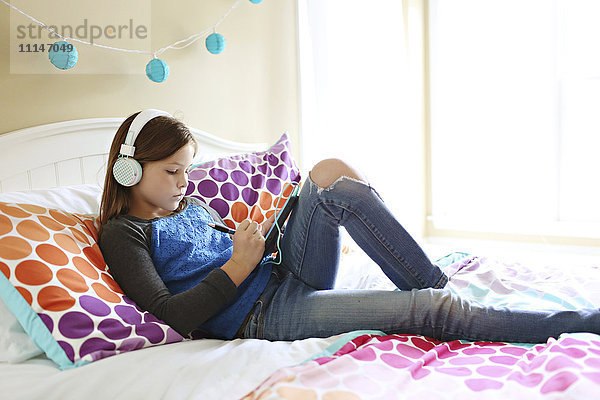 Mädchen hört Kopfhörer mit digitalem Tablet auf dem Bett