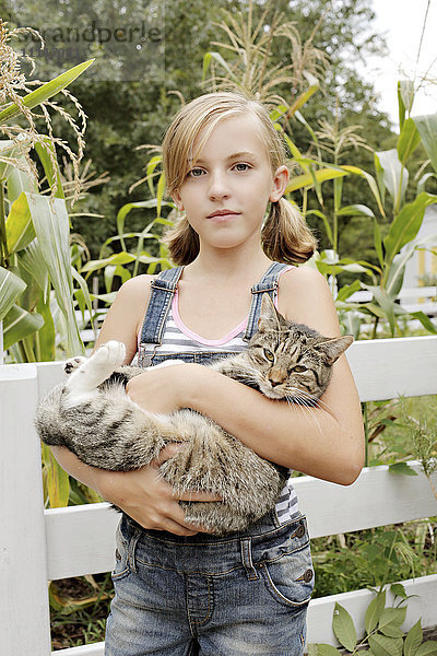 Seriöses Mädchen hält Katze im Garten