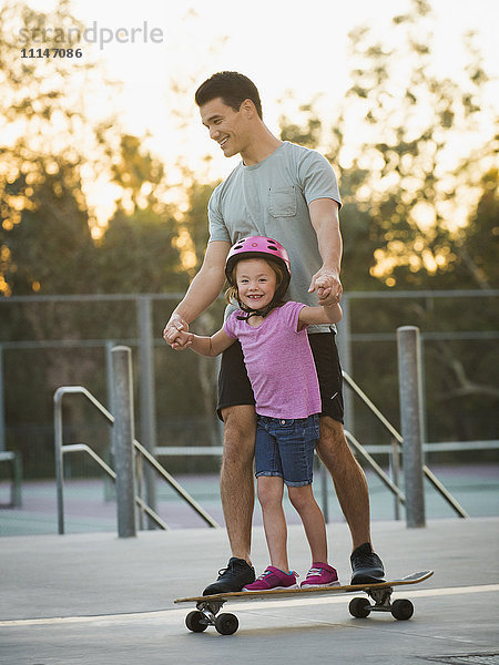 Vater und Tochter fahren Skateboard im Park
