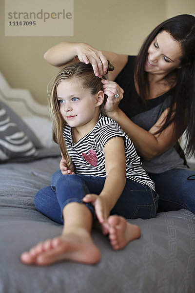 Mutter stylt die Haare ihrer Tochter auf dem Bett