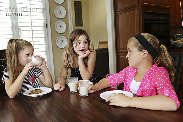 Schwestern essen Kekse mit Milch am Tisch