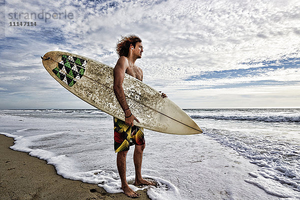 Kaukasischer Mann hält Surfbrett in den Wellen am Strand