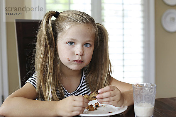 Mädchen isst Keks auf einem Tisch