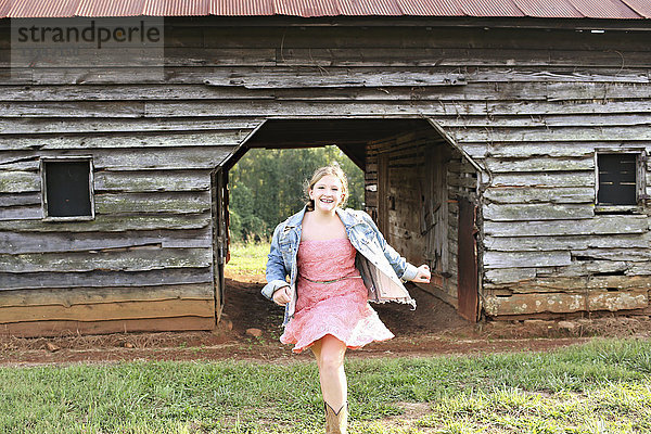 Lächelndes Mädchen läuft in der Nähe einer Scheune auf einem Bauernhof
