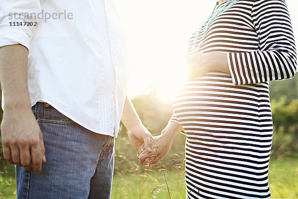 Schwangere kaukasische Paar hält Hände im Feld