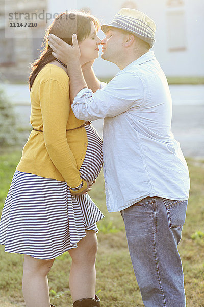 Schwangeres Paar küsst sich auf einem sonnigen Feld