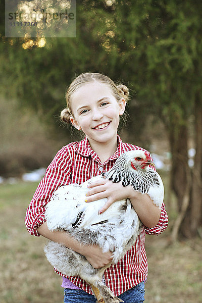 Kaukasisches Mädchen hält Huhn auf dem Bauernhof