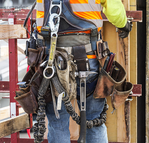 Hispanischer Arbeiter mit Werkzeuggürtel auf einer Baustelle