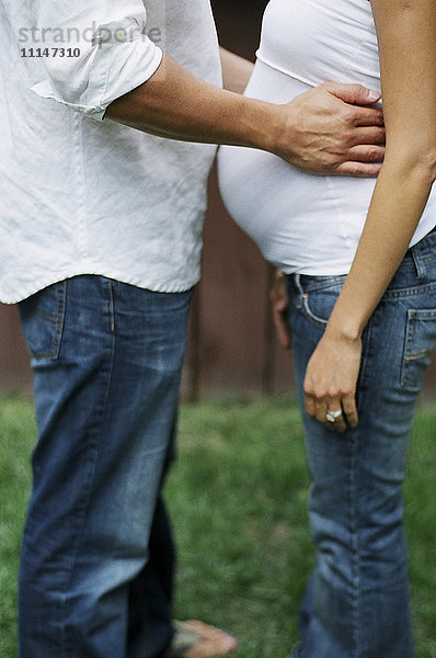 Nahaufnahme eines Mannes  der seine schwangere Frau im Hinterhof umarmt