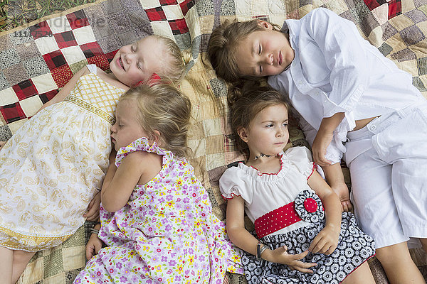 Kaukasische Kinder liegen auf einer Decke im Freien
