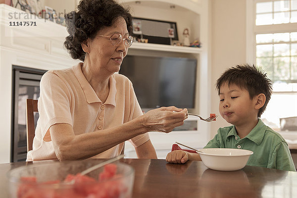 Asiatische Großmutter füttert Enkel am Tisch
