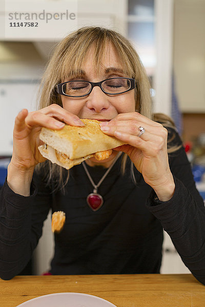 Kaukasische Frau isst Sandwich in der Küche
