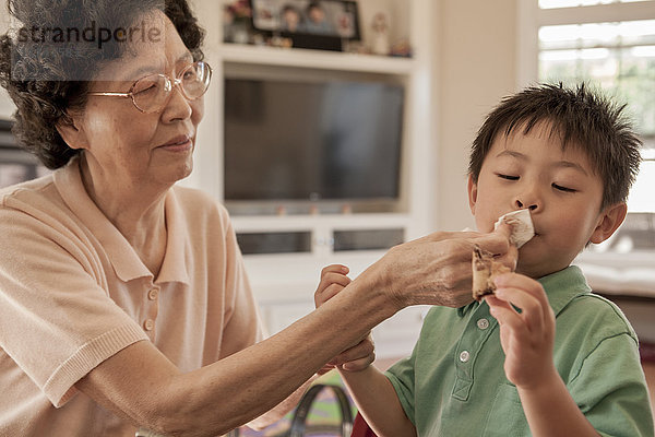 Asiatische Großmutter wischt dem Enkel am Tisch das Gesicht ab