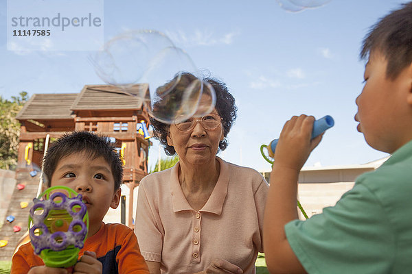 Asiatische Großmutter und Enkel beim Blasen von Seifenblasen im Freien